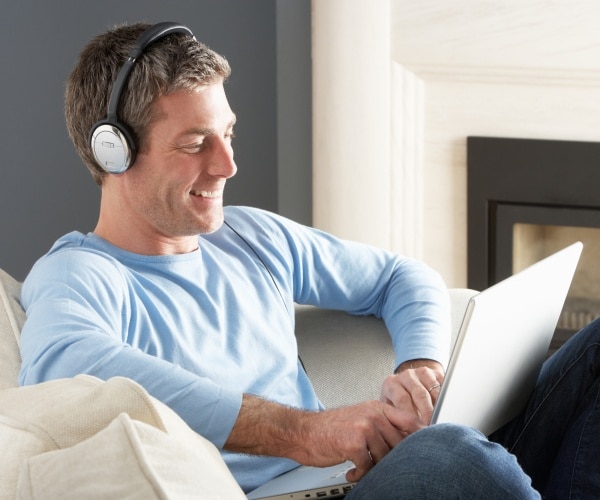 man sitting in chair with headphones on and smiling while looking at laptop