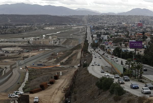 u.s. border patrol agents, lower left, stand guard on the u.s. side of the border wall.