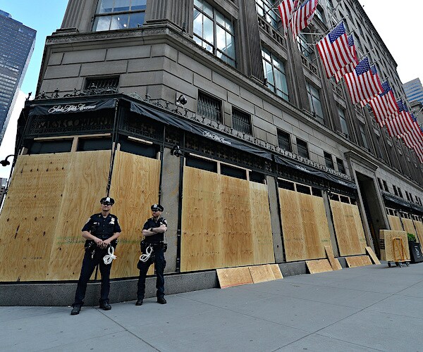 2 NYPD officers stand by as carpenters board up Saks Fifth Avenue as a precaution of riots and looters