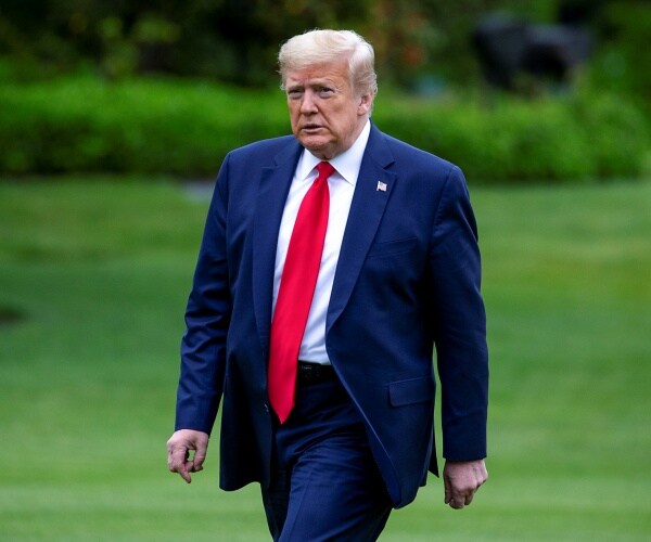 trump walking on the white house lawn in a suit and red tie