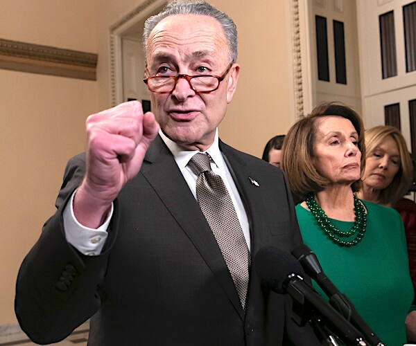 chuck schumer pumps his fist in a show of defiance or strength with nancy pelosi in the background