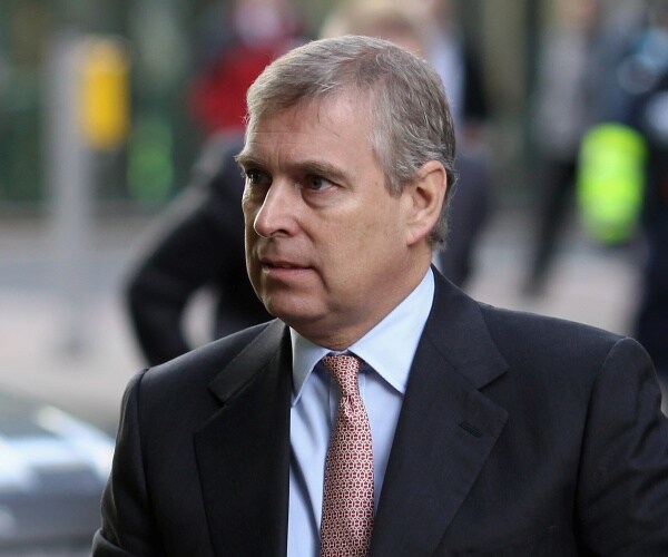 prince andrew in a black suit light blue shirt and patterned red and white tie standing outside