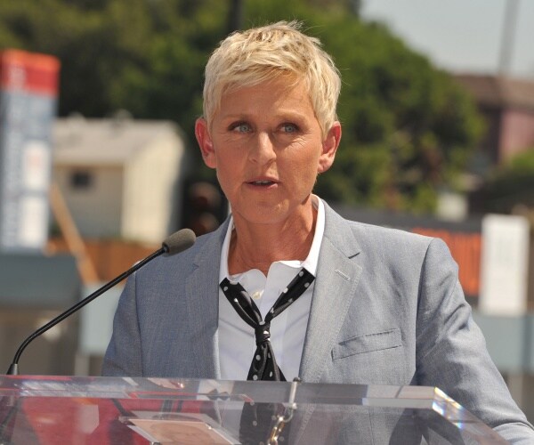 ellen degeneres in a light gray blazer white shirt and black patterned tie speaking outside at a podium