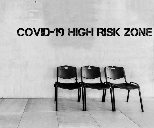 Sign that reads "COVID-19 HIGH RISK ZONE" with three chairs underneath it