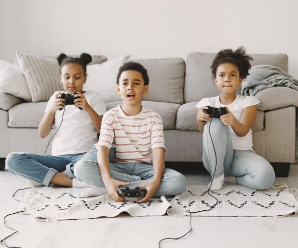 2 girls and a boy sitting on floor in front of couch playing video games