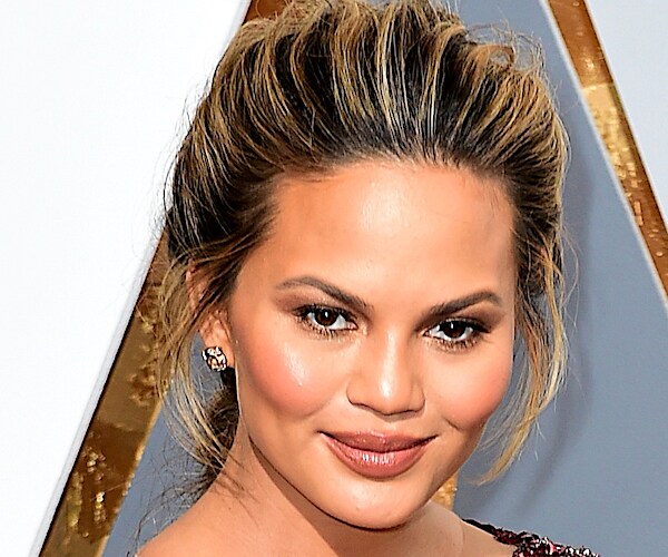 Chrissy Teigen looks down slightly and smiles wide on the red carpet