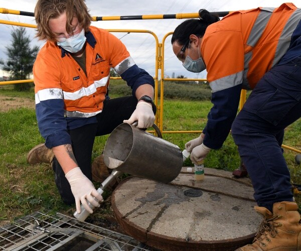 hydrographers in orange and blue uniforms take samples of sewage 