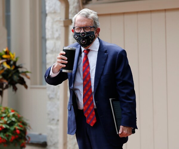 ohio governor mike dewine waves to the camera wearing a mask and holding a cup of coffee