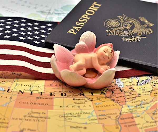 a photo illustration of a baby doll laying on an american map with an american passport and an american flag