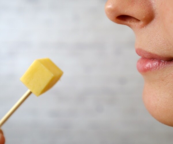 close up of woman's face, about to eat a cube of cheese on toothpick