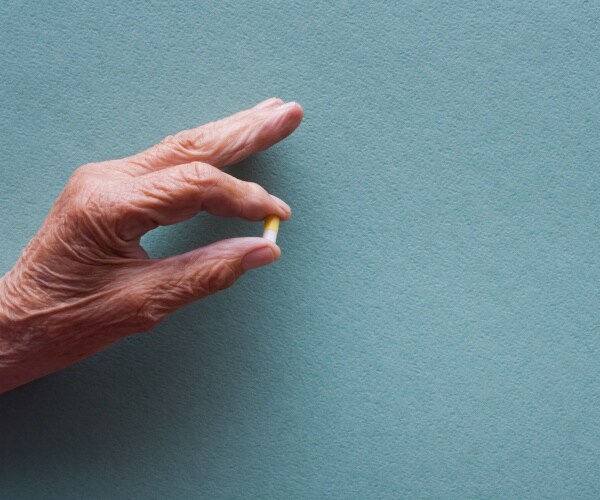 an old woman's hand holding a pill