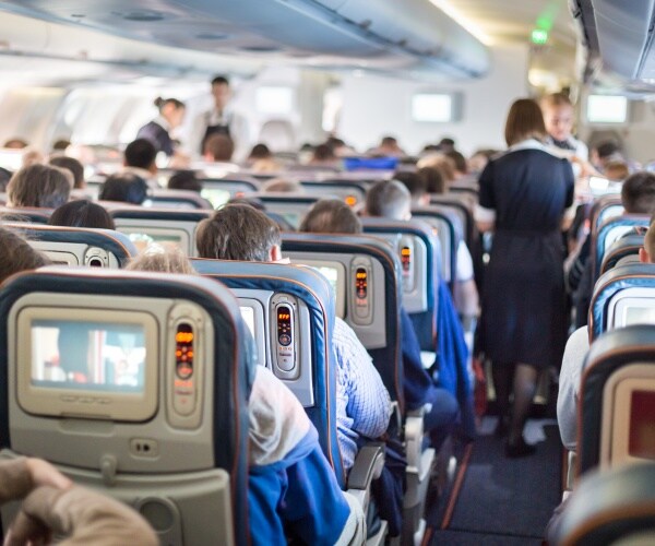 interior of plane with people in seats, flight attendants in aisles