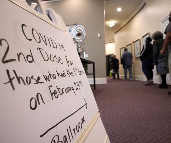 a sign in the foreground mentions a second dose of vaccine while people line up in the hall