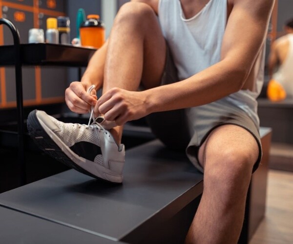 man puting sneakers on in locker room at gym