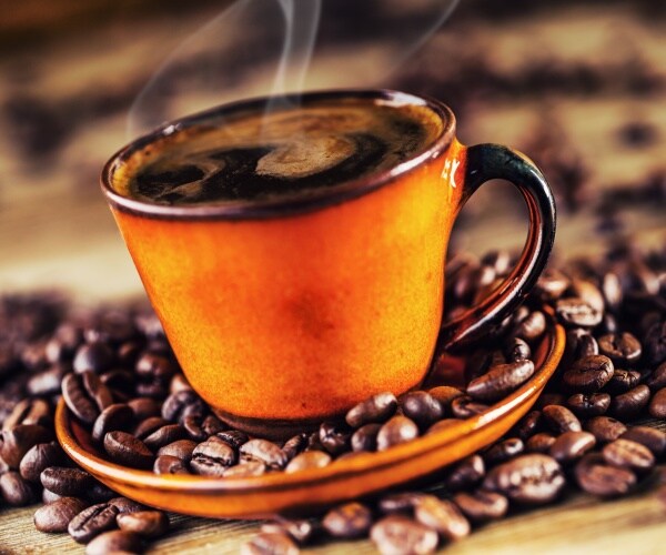 cup of steaming black coffee with coffee beans around it on table