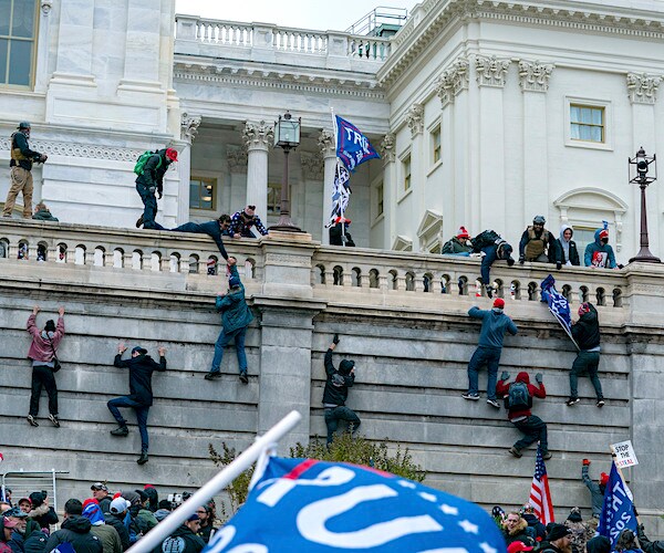 demonstrators climb the wall at the capitol building while storming the capitol