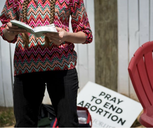 a woman reads from a bible with a sign behind her reading, pray to end abortion