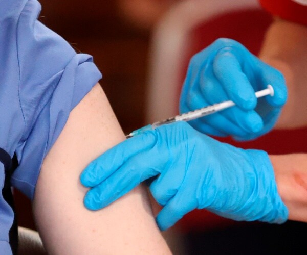 nurse wearing blue gloves vaccinates a patient with sleeves rolled up 