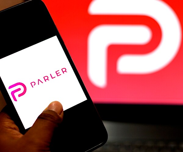 a man holds a smart phone with the parler app loading in front of the parler logo