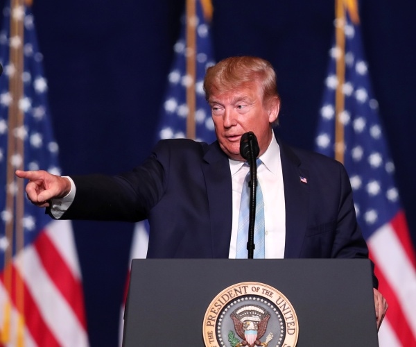 trump speaking at a podium in a navy blue suit and light blue tie