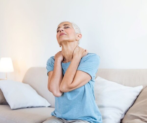 woman sitting on couch rubbing neck that is pain