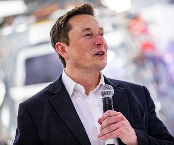 musk in a black suit and white shirt holding a mic