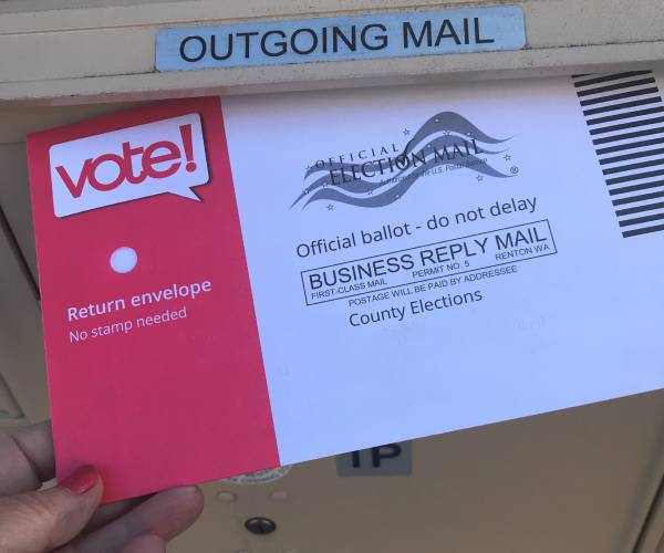 a person putting a mail in ballot in a public mail box on the street