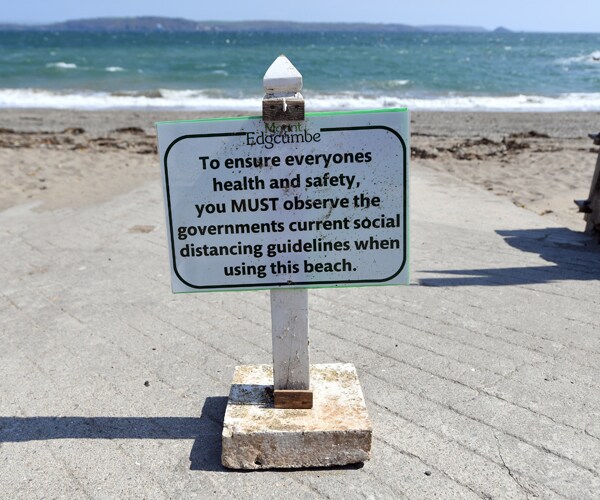 a sign at a beach in england reminding people to use social distancing