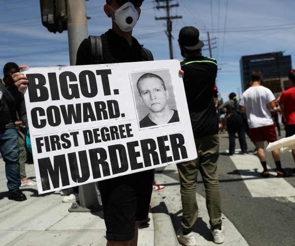 man wearing mask holds up poster board with chauvin's picture during a protest