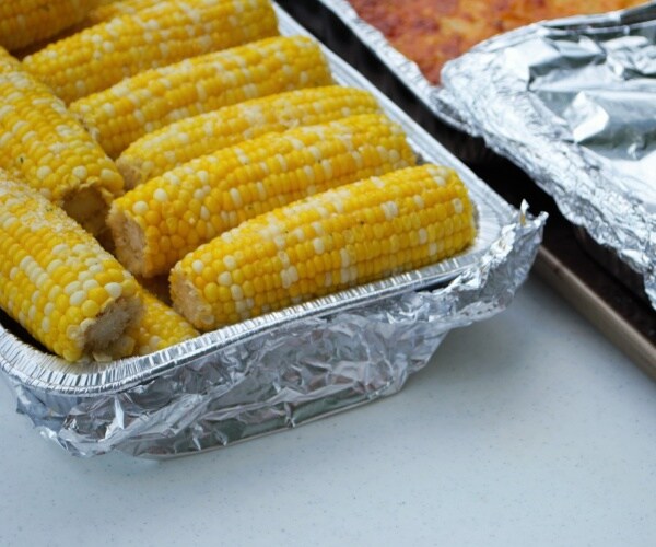 two trays of food with foil, one tray is full of corn on the cob