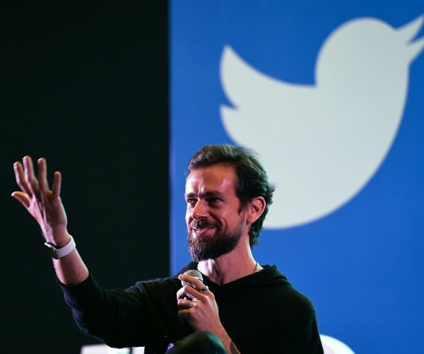 dorsey in a black hoodie speaking on stage with twitter logo projected behind him