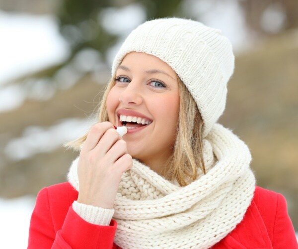 woman outside on cold winter day in coat, hat, and applying lip balm