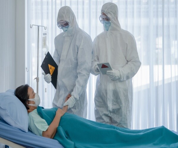 woman in hospital with covid and two doctors with protective gear talking to her