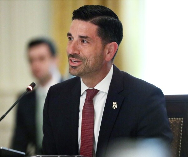 wolf in a suit and burgundy tie speaking into a small mic