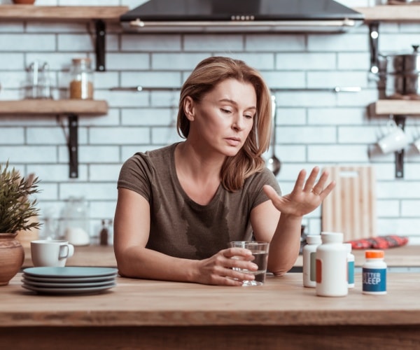 depressed woman sitting at table holding a glass of water with medications in front of her