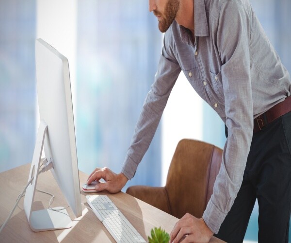 a man standing up and leaning over his computer on his desk