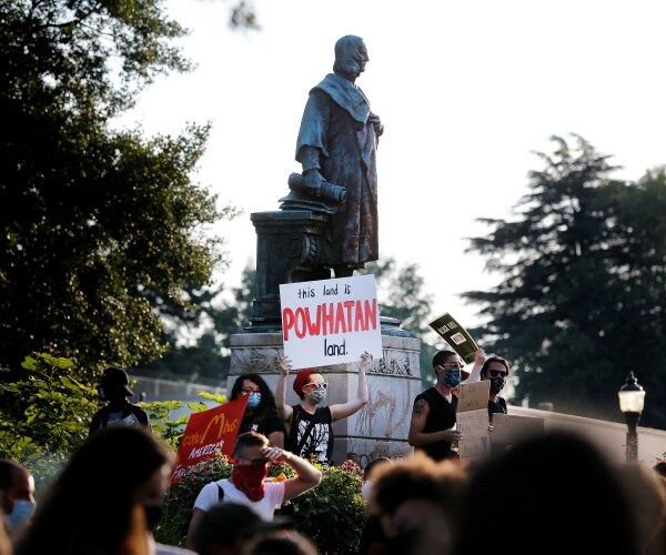 columbus statue is shown with protesters crowding around and one with a sign saying "powhatan land"