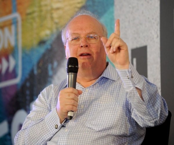 rove in a blue and white checkered shirt holding a mic