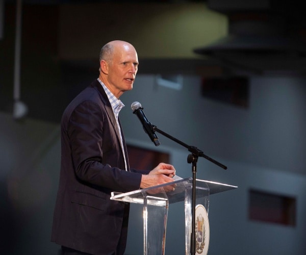 scott in a suit speaking at a clear podium