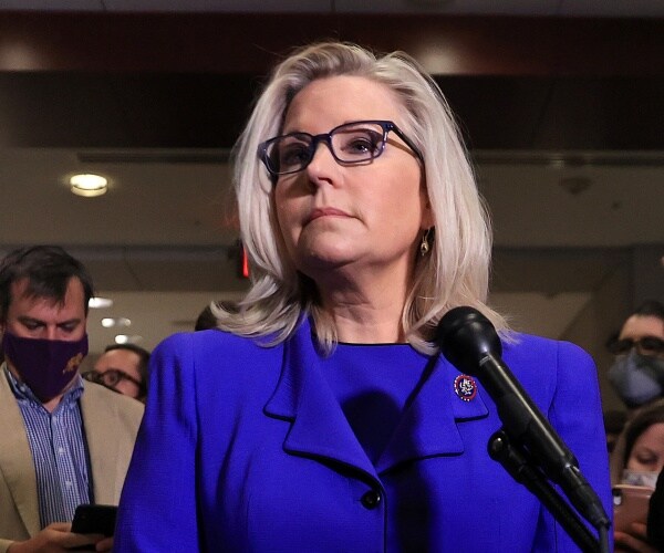 liz cheney stands next to a mic and listens.