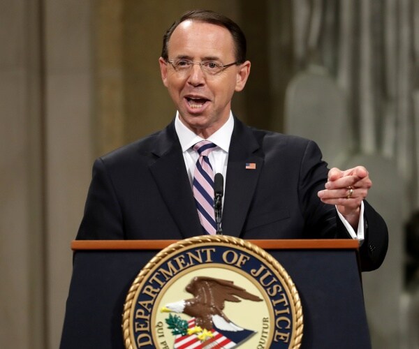 rosenstein in a black suit and pink and blue striped tie speaking to the doj