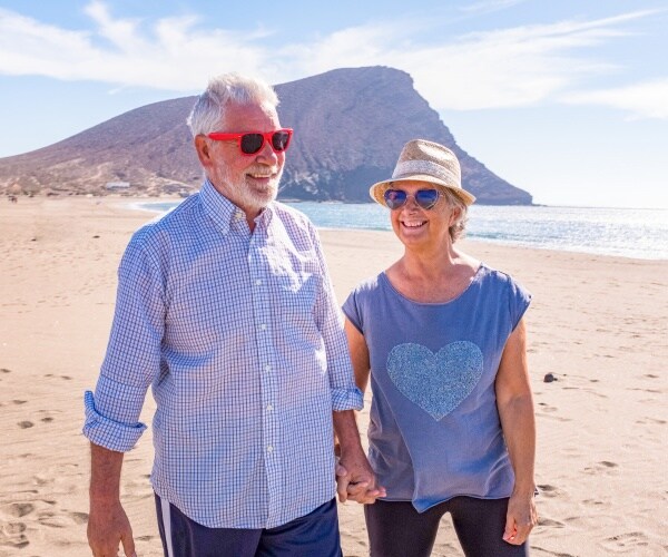 older man and woman holding hands and walking on beach