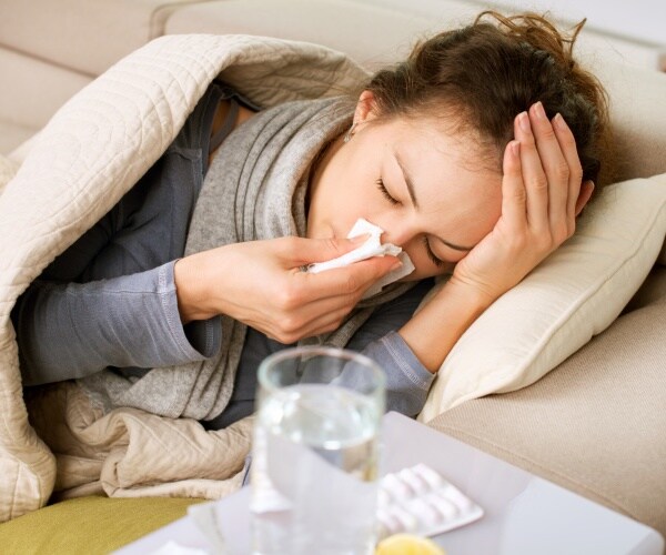 woman sick with cold, flu or virus in bed blowing nose