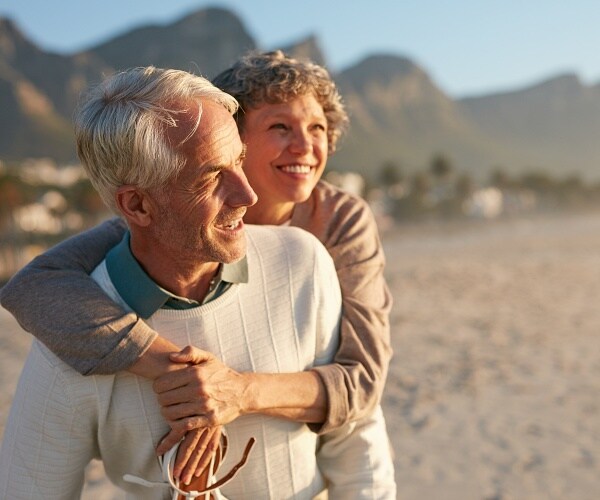 happy mature man carrying woman on his back at the beach