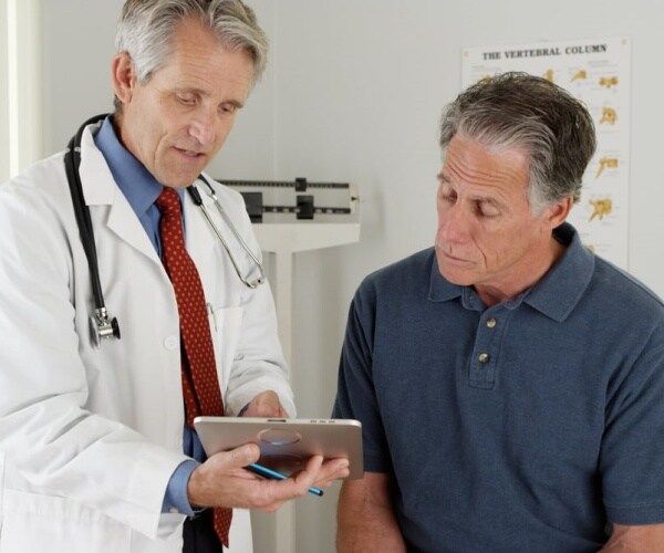 Doctor and male patient looking at tablet together in exam room