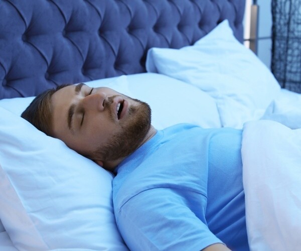 man wearing a light blue t shirt sleeping in bed with his mouth open