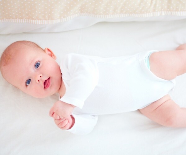 baby in crib with nothing in it looking at camera