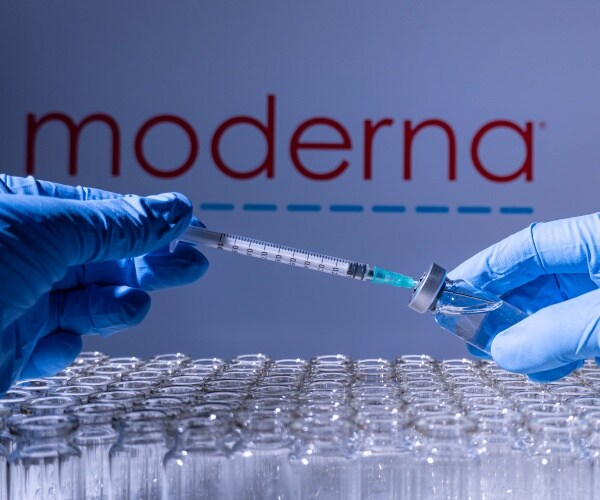 Moderna name behind vials of vaccine and a syringe