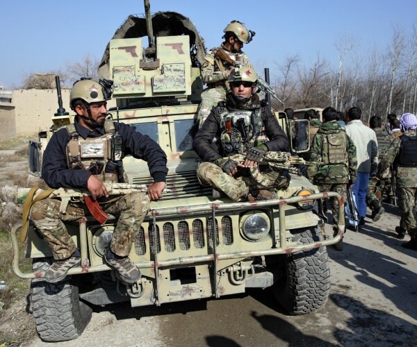 afghan forces on a military vehicle with a crowd of people walking by 