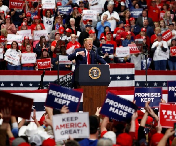 trump speaking in the middle of a rally with supporters holding up signs in support